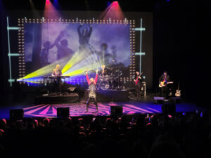 Aly Fowler on stage with her arms stretched up to the sky at the end of a song that she performed.