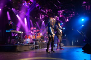 Scott Carne and Ally Fowler singing a duet together on stage with a band behind them.