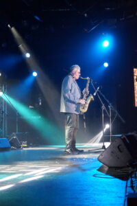 Wilbur Wilde standing on stage under blue lights playing his saxophone.